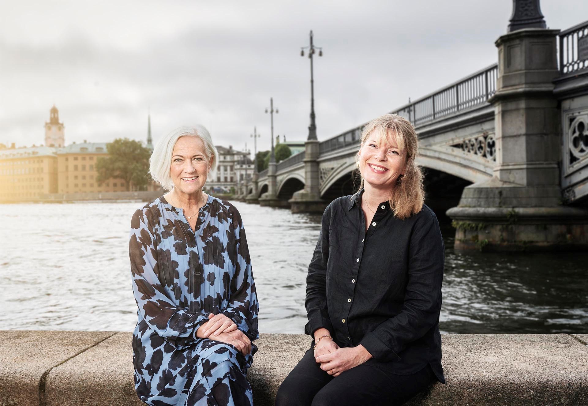 Sjukvårdsminister Acko Ankarberg Johansson och generalsekreterare Christine Cars-Ingels sitter på muren med Stockholms ström i bakgrunden. 